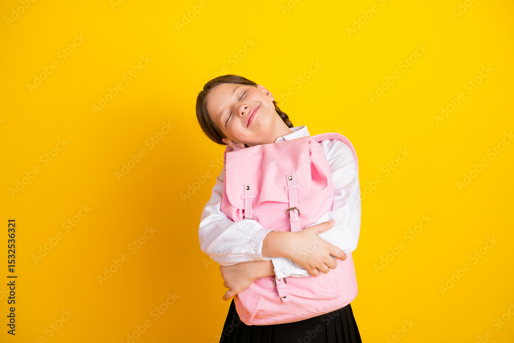 Adorable schoolgirl hugging her pink backpack with a cheerful face, isolated on a vibrant yellow background Adorable schoolgirl hugging her pink backpack with a cheerful face, isolated on a vibrant yellow background