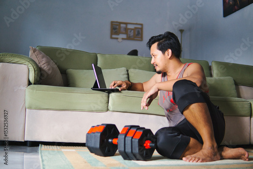Man Using Tablet At Home While Exercising With Adjustable Dumbbells
