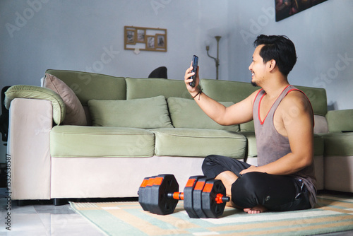 Man Using Smartphone While Exercising At Home With Dumbbell Nearby