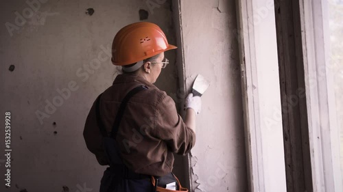 Female builder or repair worker removing old painted from wall. House renovation and renewal