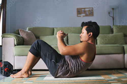 Man Exercising at Home Performing Crunches Near Sofa and Dumbbells