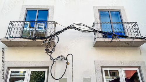 Tangled wires whimsically unite two balconies, symbolizing connectivity during Dia de la Raza in a quirky architectural dance
