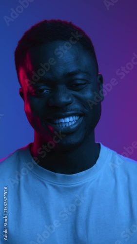 Happy Portrait of Black Man Looking at Camera and Smiling in Colorful Neon Lighting. Close Up View on African American Person and Charming Grin with White Teeth. Carefree Modeling Pose in Shoot Indoor