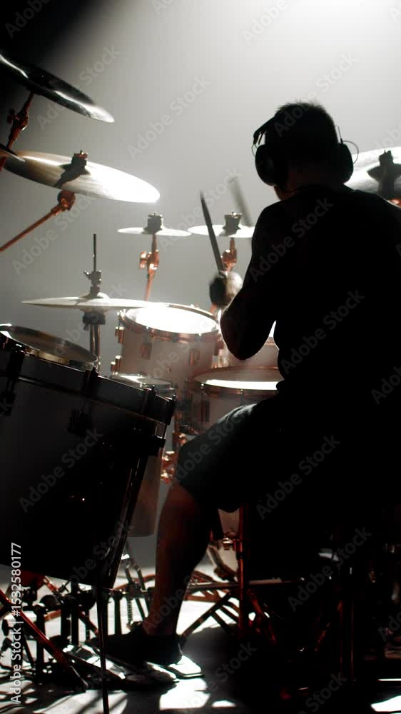 Professional drummer rehearsing alone in dark garage, back view of brawny man sitting at drum kit. Beating out rhythm of new song, creating new musical style, male silhouette against bright light