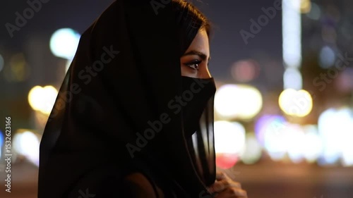 Mysterious woman in black niqab with city lights as background for islamic concept