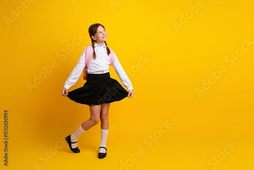 Charming Schoolgirl Twirling in Uniform on Yellow Background Showing Happiness and Excitement for a New School Year