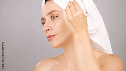 Woman using hydrating serum for skincare, applying cosmetics to enhance glow and transform her complexion. Model in a studio, dermatology benefits of hyaluronic acid for facial beauty. Grey background