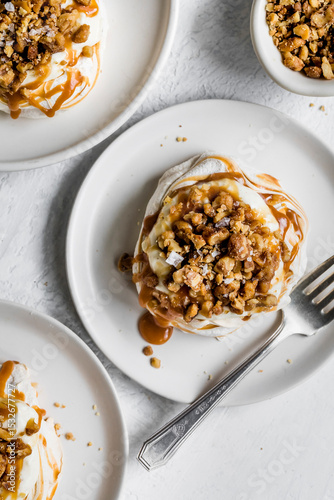 A top view of a dessert featuring meringue topped with caramel sauce and crunchy nuts, served on a white plate with a fork.