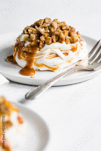 A dessert featuring meringue topped with nuts and caramel sauce on a white plate with a fork beside it.