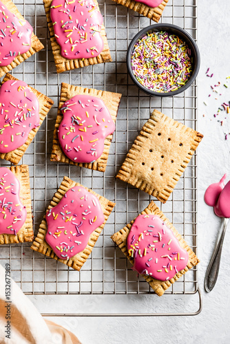 Homemade pastries with pink icing and colorful sprinkles on a cooling rack.