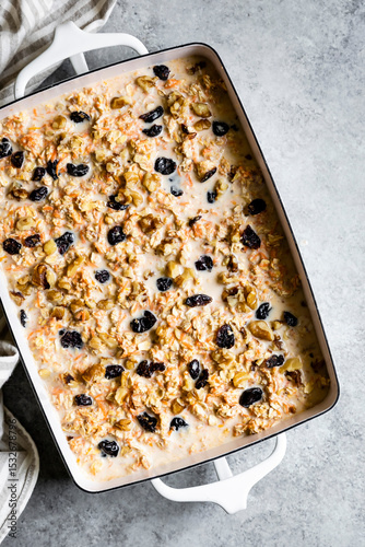 A baking dish filled with a mixture of oats, nuts, dried fruits, and milk, ready to be baked.