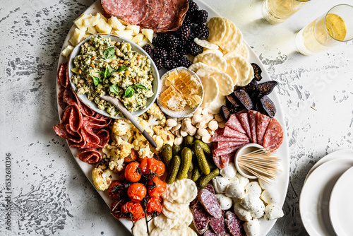 An elegant charcuterie board featuring a variety of meats, cheeses, fruits, and nuts, accompanied by crackers and a bowl of dip, set on a textured surface.