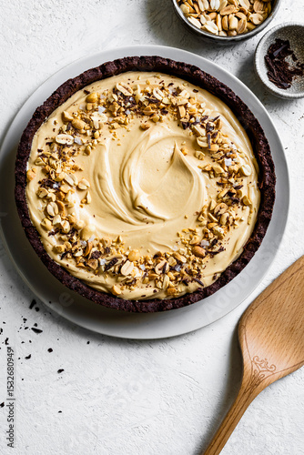 A creamy peanut butter pie with a chocolate crust, topped with chopped peanuts and chocolate shavings, served on a white plate.