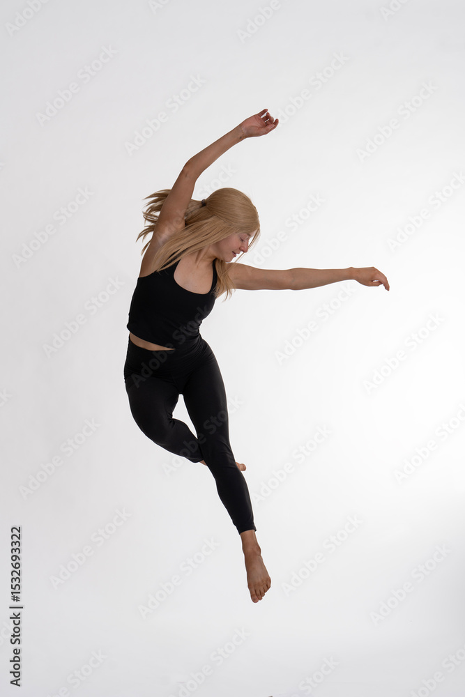 Fototapeta premium Dancer Toni in the studio dancing with motion and light - The image depicts a dancer captured mid-air in a striking pose. They are dressed in a black tank top and black leggings