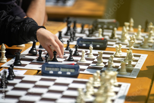 People's hands moving chess pieces on sunlit boards during an outdoor park game on a summer day
