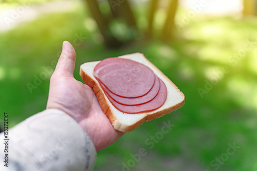 Hand holding a square slice of toasted white bread topped with three round pieces of smoked and boiled beef