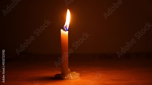 Candle burning softly on a wooden surface in dim light  