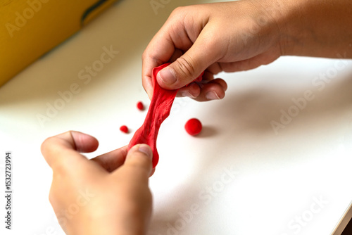 Child’s hands modeling red air dry clay, promoting creativity, sensory development, and fine motor skills. Perfect for summer activities and playful learning.