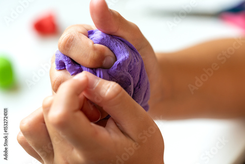 Close-up of child squeezing soft purple modeling clay in hands. Creative summer activity, sensory development, and fun for kids. Selective focus.