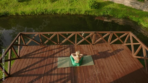woman practicing yoga during sunrise on a terrace of a remote cabin in the woods with a lake view