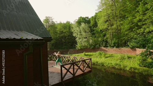 woman practicing yoga during sunrise on a terrace of a remote cabin in the woods with a lake view