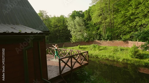 woman practicing yoga during sunrise on a terrace of a remote cabin in the woods with a lake view