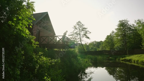 woman enjoying beautiful lake and forest view from the terrace of a wooden cabin during sunrise