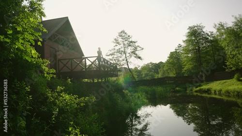woman enjoying beautiful lake and forest view from the terrace of a wooden cabin during sunrise