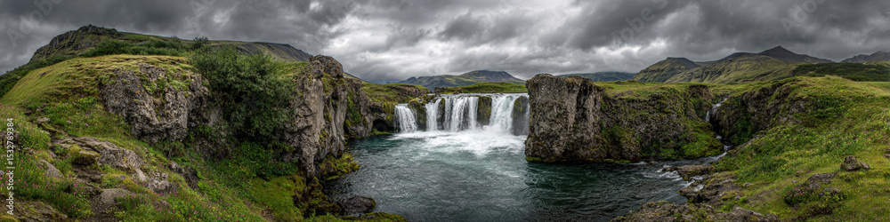 Obraz premium Panoramic view of a scenic waterfall flowing between rocky cliffs under a cloudy sky landscape view