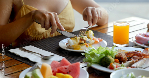 Person enjoying healthy breakfast with eggs Benedict, salad, fruit, and orange juice at outdoor cafe. Fresh, nutritious morning meal concept. Slow motion