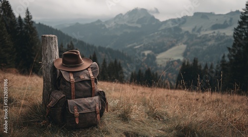 A weathered leather backpack and hat rest beside a worn wooden post overlooking a vast, misty mountain range and autumnal valley