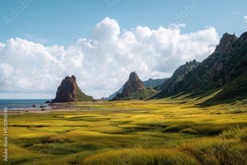Sunlit coastal grassland expanse, featuring two prominent rock formations and a mountainous backdrop under a partly cloudy sky