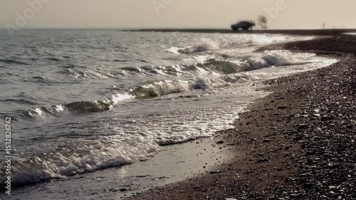 The car stands on the shore of the sea or lake in the rays of the sunset against the backdrop of calm waves.