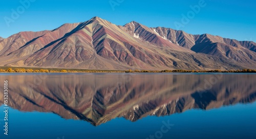 Striped mountains reflected in a calm lake under a clear blue sky