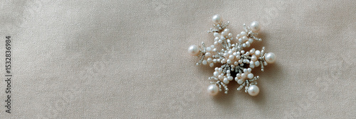 Elegant pearl brooch in snowflake shape lying on textured beige fabric background