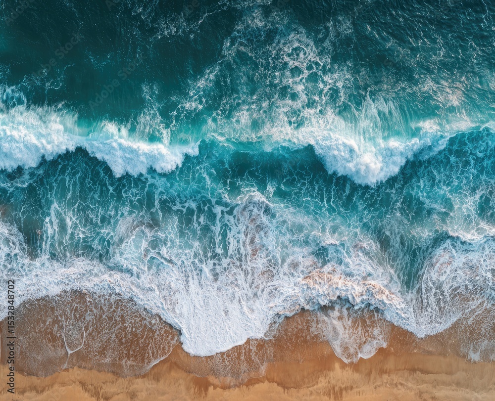 Fototapeta premium Aerial view of ocean waves crashing on a sandy beach, displaying a vibrant turquoise and white contrast