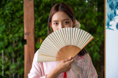 Beautiful young Japanese woman dressing in traditional kimono or yukata costume covering half face with fan