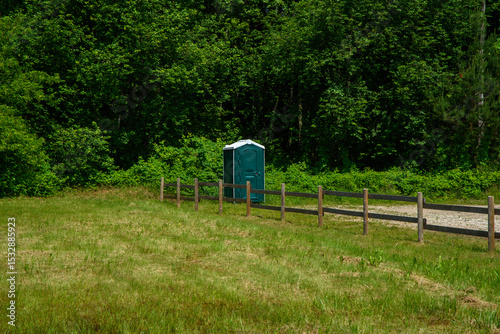 Принти на полотні A lone portable toilet stands by a wooden fence in a grassy field, with dense gr