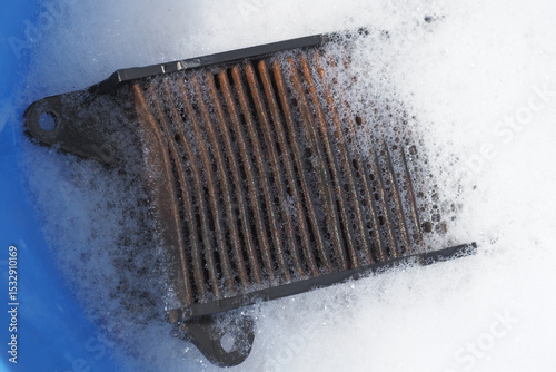 Cleaning old dirty dust air filter from moped in soapy water inside a blue bucket.