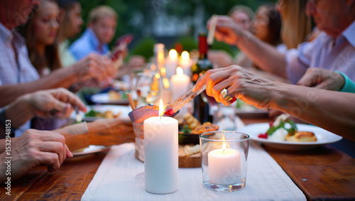 close-up of an outdoor dinner, a table covered with a white tablecloth, with various snacks, glasses, bottles and lit candles. The hands of people sitting at the table are visible.