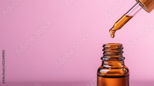 A clear pipette is gently squeezing drops of essential oil into an amber glass bottle. The vibrant pink background highlights the rich color of the oil, perfect for skincare
