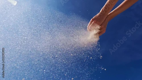 Woman pouring sand from hand on beach, blue sky.