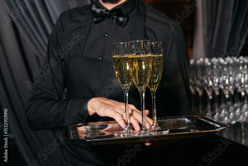 Waiter serving champagne flutes at formal event. A waiter in black attire carries a tray with glasses of champagne during a formal celebration or upscale gathering.