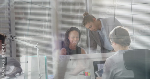 Collaborating worker in black dress reviewing monitor with coworker in office, with pen holder
