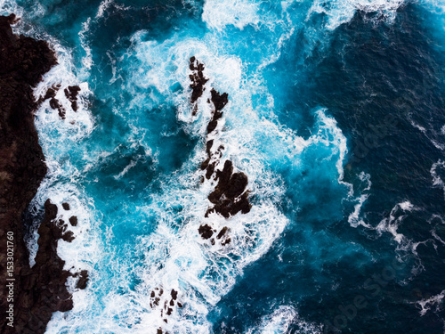 Blue turquoise water surface top down aerial drone shot of waves crushing into cliffs near Madeira island Portugal