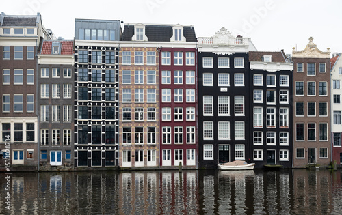 Traditional dutch houses reflecting on amsterdam canal on cloudy day