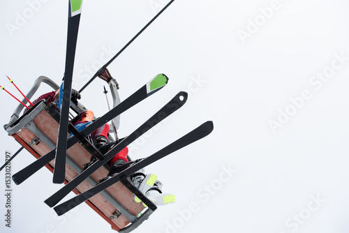 Skier ascending on chairlift with ski equipment on cloudy winter day