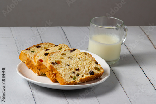 Slices of Traditional Sweet Fruit Bread and a glass of milk on a Wooden Board