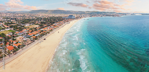 Fototapeta Naklejka Na Ścianę i Meble -  Stunning coastline with houses, hotels, and crystal clear turquoise water meeting sandy beach under a vibrant sunset sky