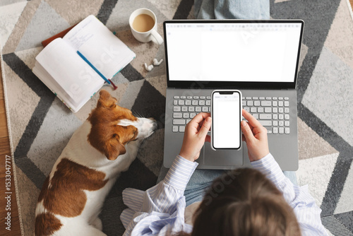 Young woman sitting at home with a laptop and working or studying remotely from home while her Jack Russell Terrier dog relaxes beside her